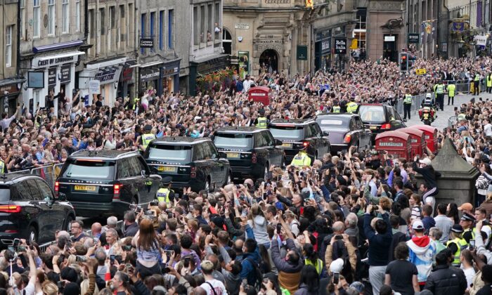 Crowds watch as the hearse carrying the coffin of Queen Elizabeth II, draped with the Royal Standard of Scotland, passes Mercat Cross in Edinburgh, Scotland, on Sept. 11, 2022. (Ian Forsyth/PA Media)

