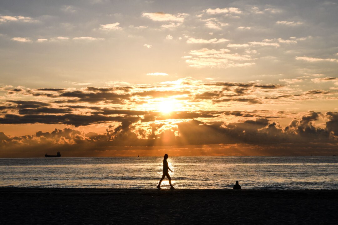 A woman walks during a sunrise on the beach in Miami Beach, Fla., on March 23, 2021. (Chandan Khanna/AFP via Getty Images)