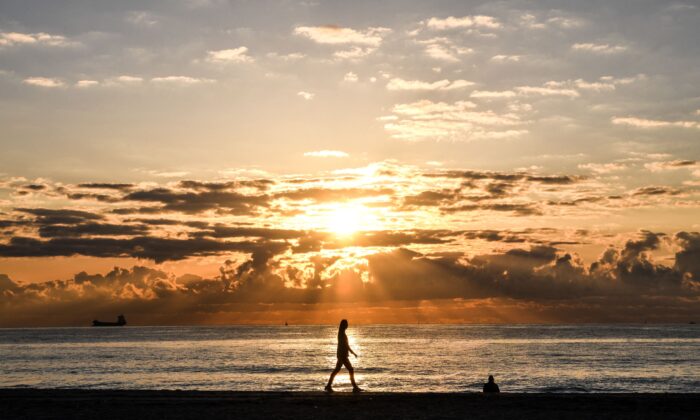 A woman walks during a sunrise on the beach in Miami Beach, Fla., on March 23, 2021. (Chandan Khanna/AFP via Getty Images)