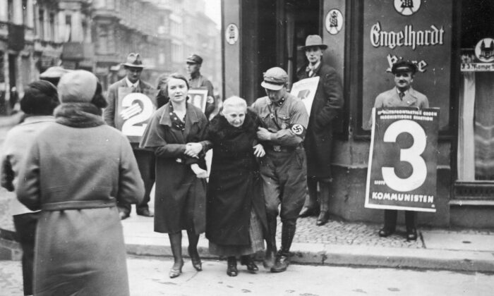A Nazi Party member helps an elderly women from a polling station during the German federal election, Berlin, in November 1932. On the right is a man holding a placard for the Communist Party of Germany (KPD). (FPG/Archive Photos/Getty Images)
