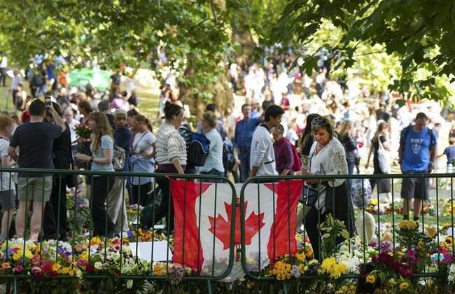 Long lines of mourners lay flowers near a Canadian flag as people wait to pay their respects to Queen Elizabeth II near the gates of Buckingham Palace in London on  Sept. 11, 2022. ( The Canadian Press/Nathan Denette）