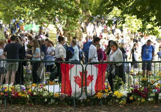 Long lines of mourners lay flowers near a Canadian flag as people wait to pay their respects to Queen Elizabeth II near the gates of Buckingham Palace in London on Sept. 11, 2022. ( The Canadian Press/Nathan Denette)