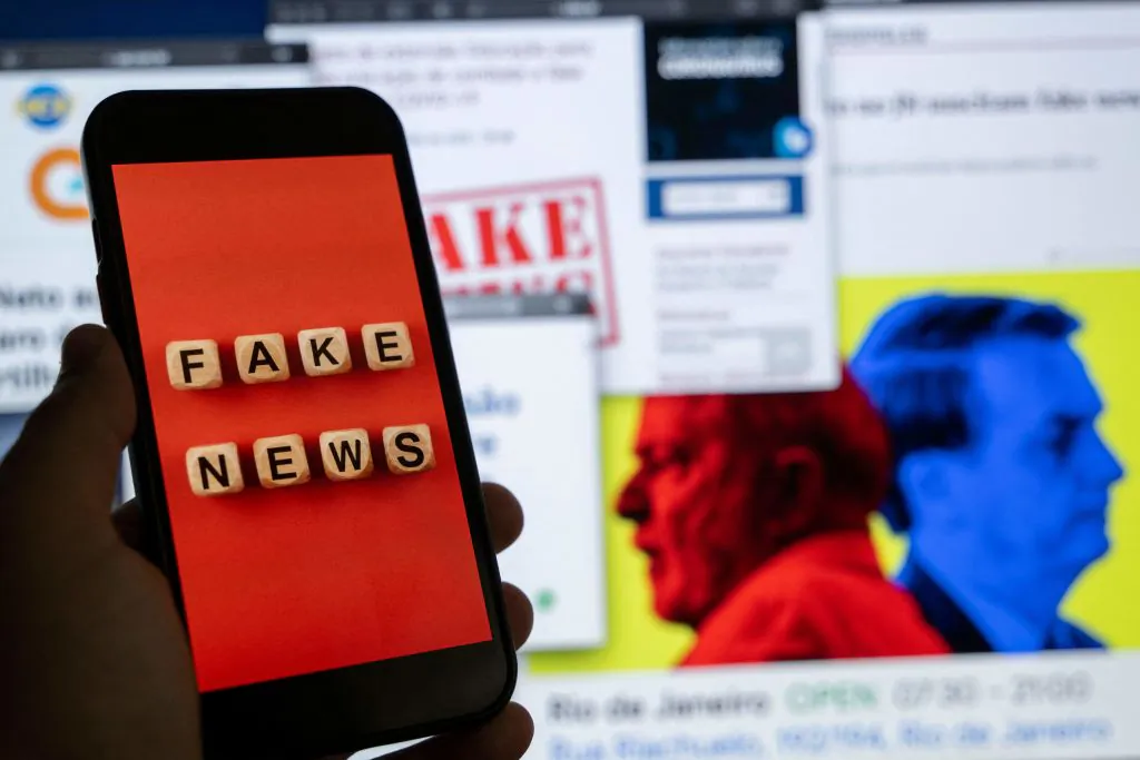 An illustration shows a smart phone screen displaying the phrase "Fake News" in front of a desktop screen showing several news and research reports about fake news and disinformation related to the upcoming Brazilian presidential election, in Rio de Janeiro, Brazil, on Aug. 29, 2022. (Mauro Pimentel/AFP via Getty Images)