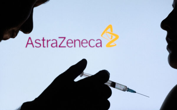 People pose with syringe with needle in front of displayed AstraZeneca logo