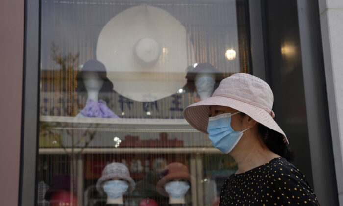 A woman wearing mask passes by mannequin heads wearing masks in a hat shop in Beijing on Sept. 9, 2022. (Ng Han Guan/AP Photo)