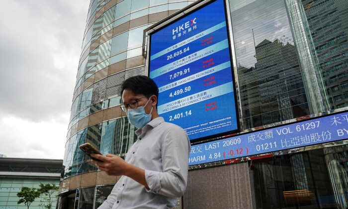 People walk past a screen displaying the Hang Seng stock index outside Hong Kong Exchanges, in Hong Kong, on July 19, 2022. (Lam Yik/Reuters)
