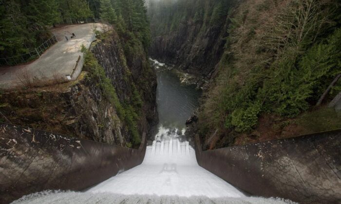 Water flows over the Cleveland Dam as people walk with a dog in Cleveland Park in North Vancouver, B.C., on Dec. 25, 2015. (The Canadian Press/Darryl Dyck)