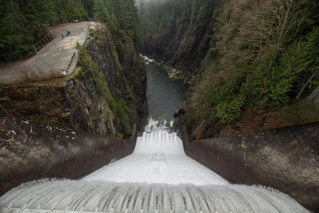 Water flows over the Cleveland Dam as people walk with a dog in Cleveland Park in North Vancouver, B.C., on Dec. 25, 2015. (The Canadian Press/Darryl Dyck)