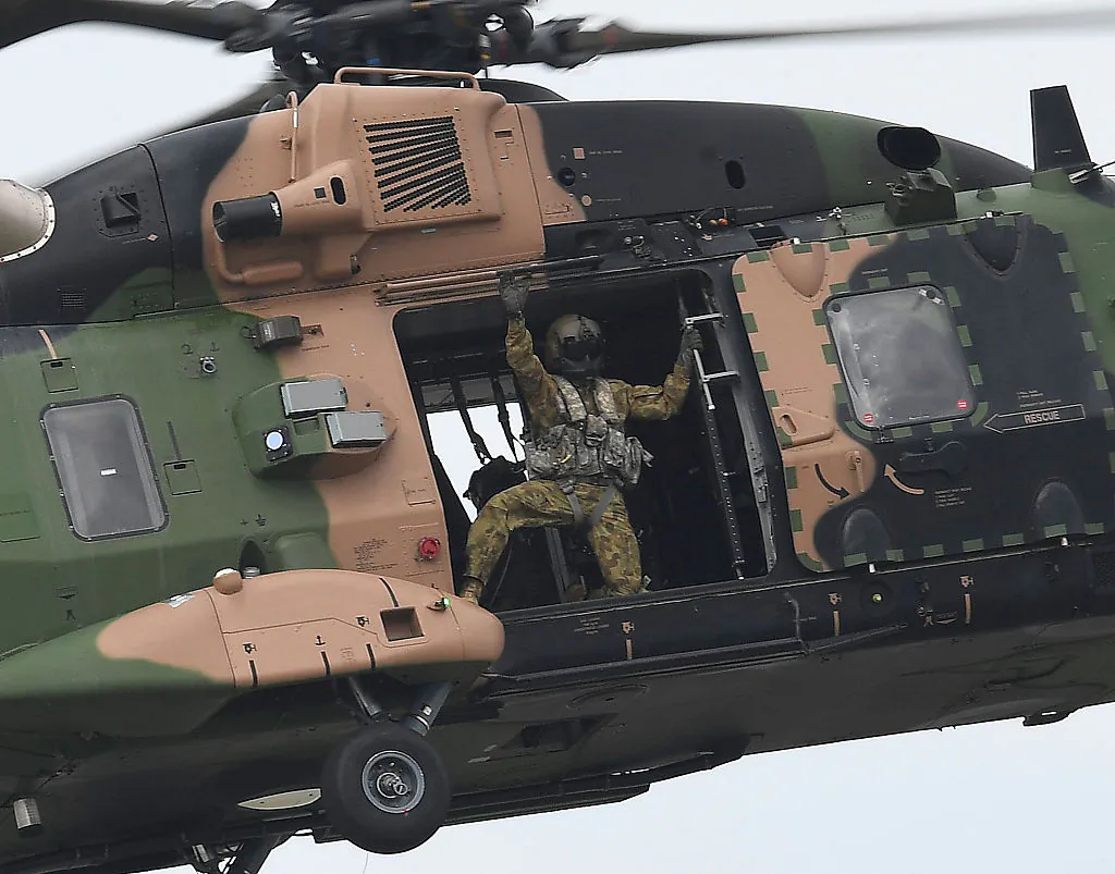 A loadmaster from an Australian Army MRH90 Taipan helicopter waves to the crowd as it performs during the T150 Defence Force Air Show in Townsville, Australia, on Oct. 15, 2016. (Ian Hitchcock/Getty Images)