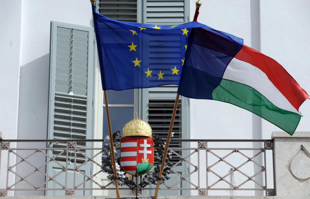 EU and Hungarian flags fly in front of a Hungarian crest at the presidental palace in Budapest, Hungary, on March 30, 2012. (Attila Kisbenedek/AFP via Getty Images)