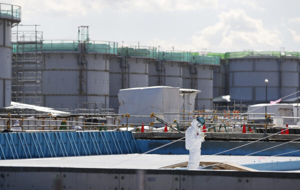A worker, wearing protective suits and masks, takes notes in front of storage tanks for radioactive water at Tokyo Electric Power Co's tsunami-crippled Fukushima Daiichi nuclear power plant in Okuma town