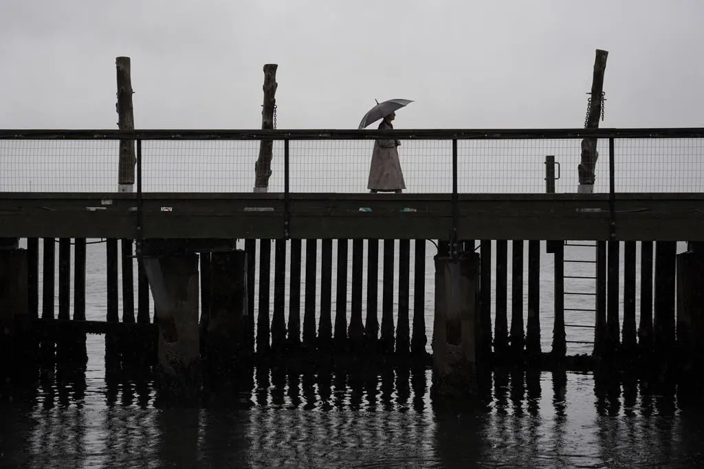 A pedestrian walks across a footbridge on the Halifax waterfront as rain falls ahead of Hurricane Fiona making landfall in Halifax on Sept. 23, 2022. (The Canadian Press/Darren Calabrese)