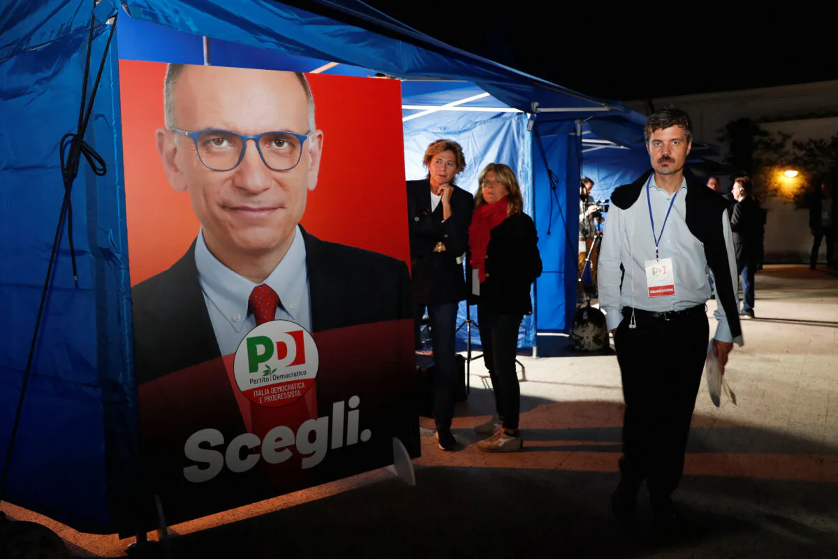 People stand next to a poster of Enrico Letta, secretary of the centre-left Democratic Party (PD), at party headquarters during the snap election in Rome, Italy, on Sept. 25, 2022. (Remo Casilli/Reuters)