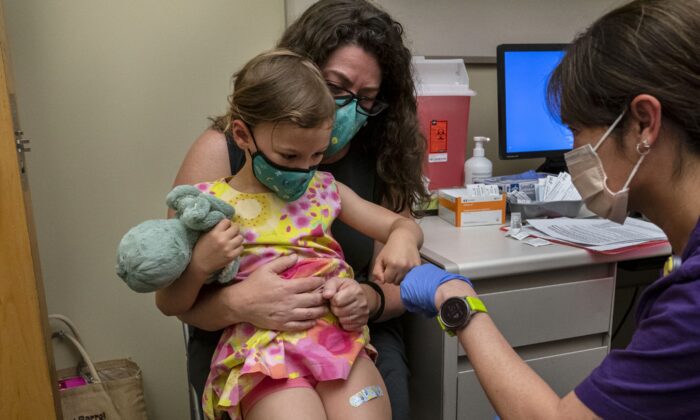 Nora Burlingame, 3, sits on the lap of her mother, Dina Burlingame, and gets a fist bump from nurse Luann Majeed after receiving her first dose of the Pfizer COVID-19 vaccination at UW Medical Center-Roosevelt in Seattle, Wash., on June 21, 2022. (David Ryder/Getty Images)