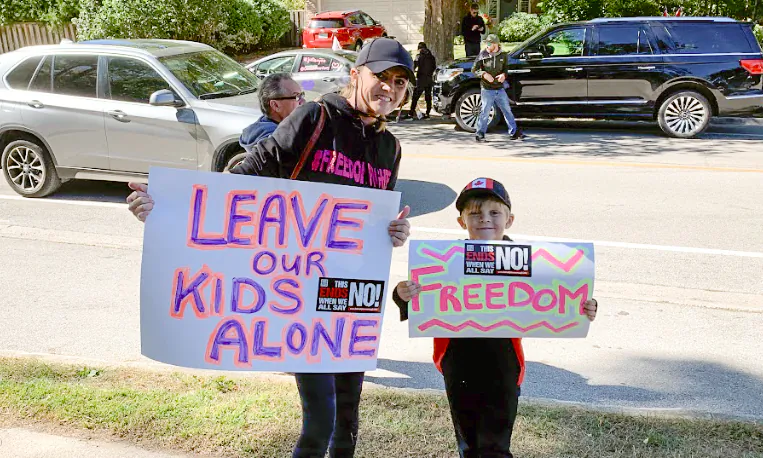 A local mother and her child protest outside Oakville Trafalgar High School on Sept. 23 against a teacher wearing large prosthetic breasts to class. (Peter Wilson/The Epoch Times)