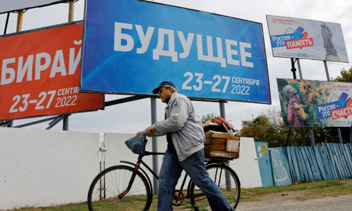 2022 年 9 月 26 日，在乌克兰扎波罗热地区的俄罗斯控制的梅利托波尔市，一名男子骑着自行车走过横幅，宣传关于俄罗斯控制的乌克兰地区与俄罗斯的联合公投。（亚历山大·埃尔莫琴科） /路透社）
