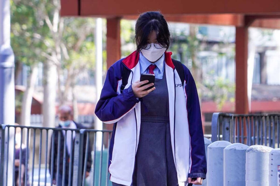 A female secondary school student in school uniform looking at her phone in Hong Kong on Jan. 20, 2022. (Adrian Yu/The Epoch Times)