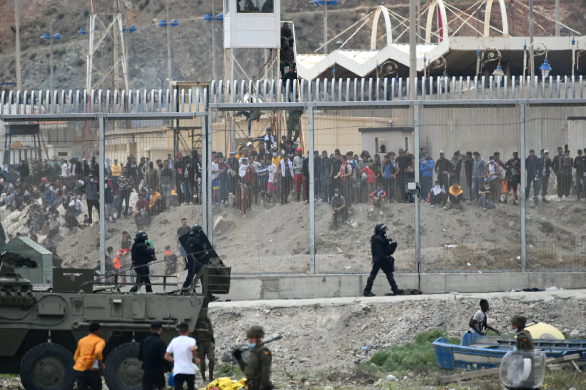 Spanish soldiers and Guardia Civil members patrol the border fence of the Spanish exclave of Ceuta, on May 18, 2021, while hundreds of African migrants seeking to breech the border stand on the other side, in Morocco. (Antonio Sempere/AFP via Getty Images)