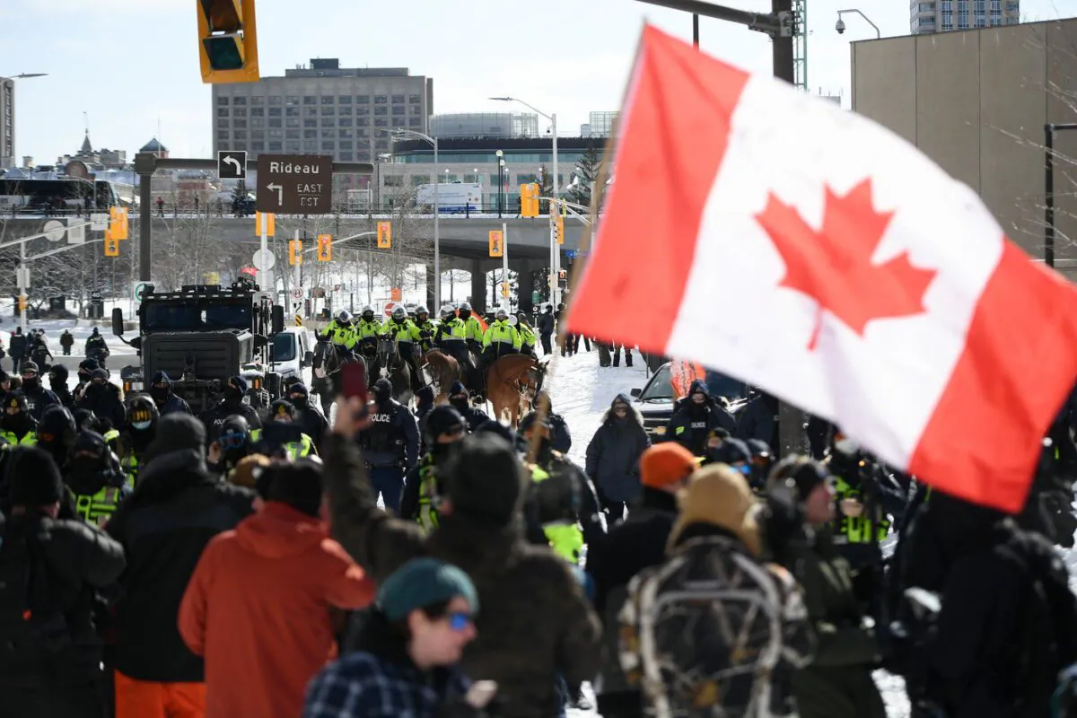 Protesters face police officers on foot and horseback and an armoured vehicle on Colonel By Drive near the truck blockade in Ottawa, on Feb. 18, 2022. (The Canadian Press/Justin Tang)