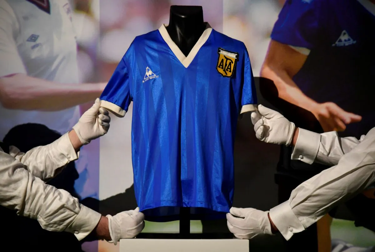 Art handlers pose with the shirt worn by Argentinian soccer player Diego Maradona in the 1986 World Cup, ahead of it being auctioned by Sotheby's, in London, Britain, on April 20, 2022. (Toby Melville/Reuters)