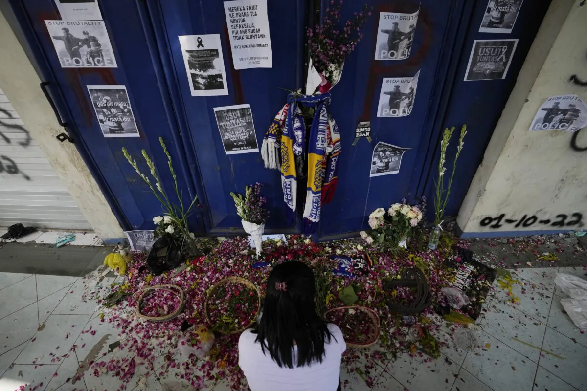 A woman takes a moment for the victims of Saturday's soccer match stampede in front of gate 13 at the Kanjuruhan Stadium in Malang, Indonesia, on Oct. 4, 2022. (Achmad Ibrahim/AP Photo)