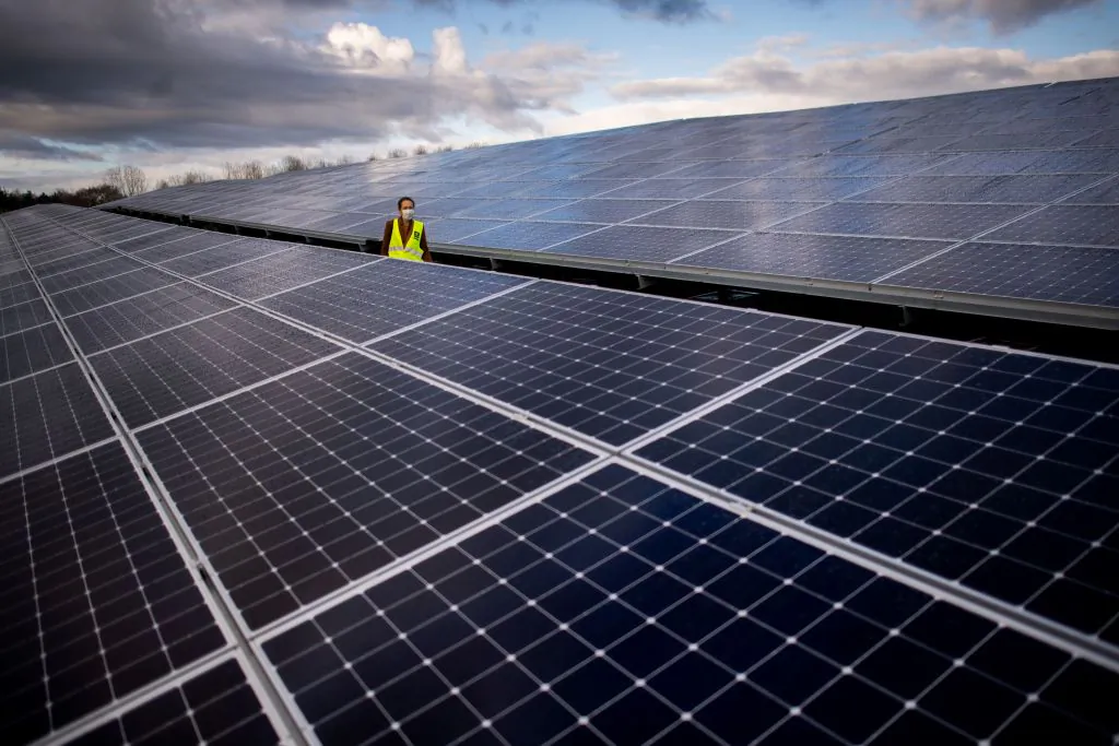 A woman walks through the solar pannels of a photovoltaic power plant installed by Generale du Soleil (GDS) and operated by Energ'iV SEML in a former landfill of waste, on Dec. 8, 2020 in Guignen, western France. (Loic Venance/AFP via Getty Images)