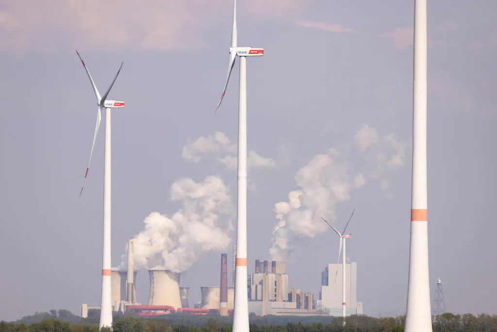 Steam rises from cooling towers of the Neurath coal-fired power plant as wind turbines spin over a field of rapeseed near Bedburg, Germany, on May 05, 2022. (Andreas Rentz/Getty Images)