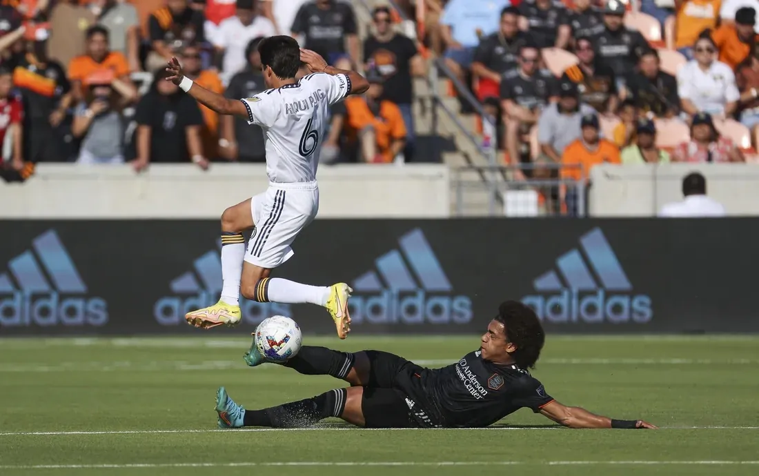 Riqui Puig of the Los Angeles Galaxy jumped over the tackle of Houston Dynamo's Adalberto Carrasquilla in Houston, Tex., on Sunday, Oct. 9, 2022. (Field Level Media)
