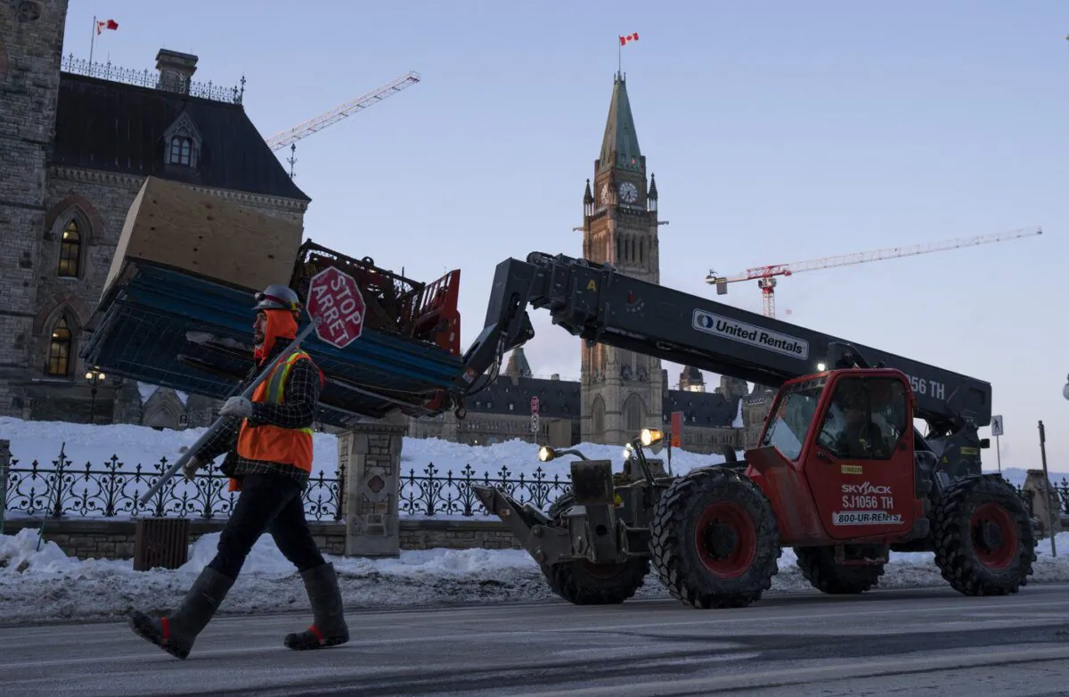 Workers use heavy equipment to remove temporary fencing and supplies from the parliamentary precinct, Feb. 23, 2022 in Ottawa. (The Canadian Press/Adrian Wyld)
