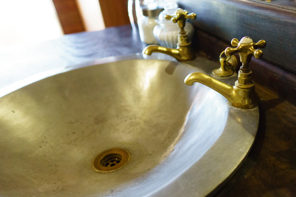 Vintage,Brass,Taps,And,Antique,Metal,Basin,On,Timber,Benchtop.