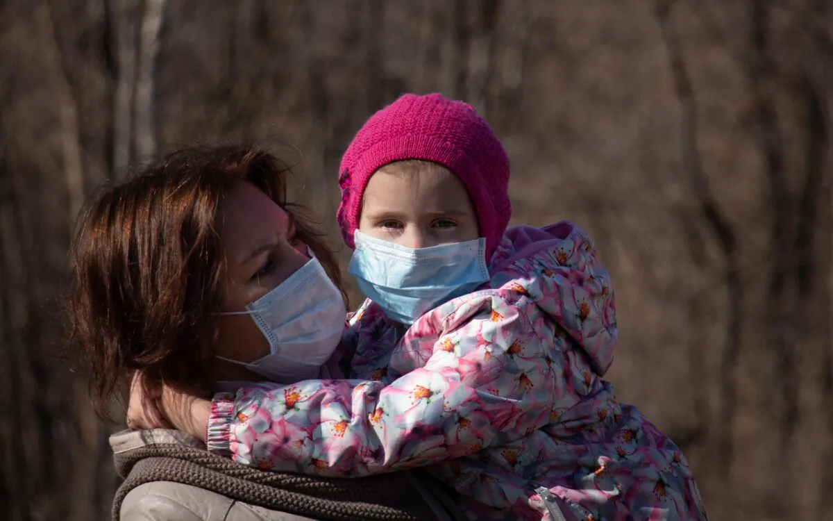 A mom holds her daughter, both wearing masks, during the coronavirus (COVID-19) pandemic, in a file photo. (Nik Anderson/Flickr, CC BY 2.0)