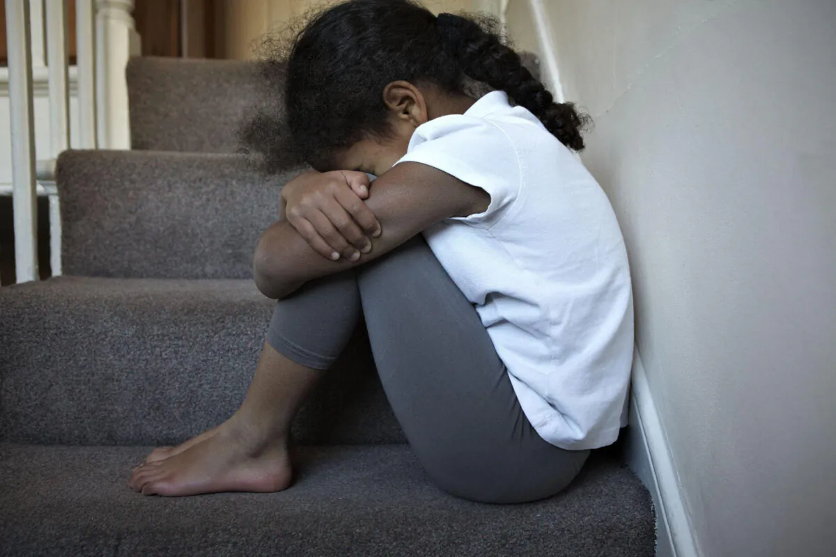 Undated photo, posed by a model, of a child sitting on some stairs in an unspecified location in England. (NSPCC/PA)