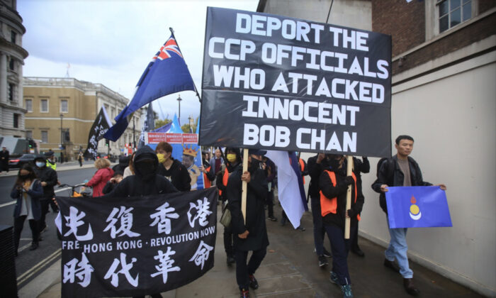 抗议者于 2022 年 10 月 23 日在英国伦敦的白厅游行，举着横幅要求将殴打陈博的中共官员驱逐出境。  Bob Chan 在 2022 年 10 月 16 日的香港民主抗议活动中被拖入曼彻斯特领事馆并遭到殴打。（Martin Pope/Getty Images）
