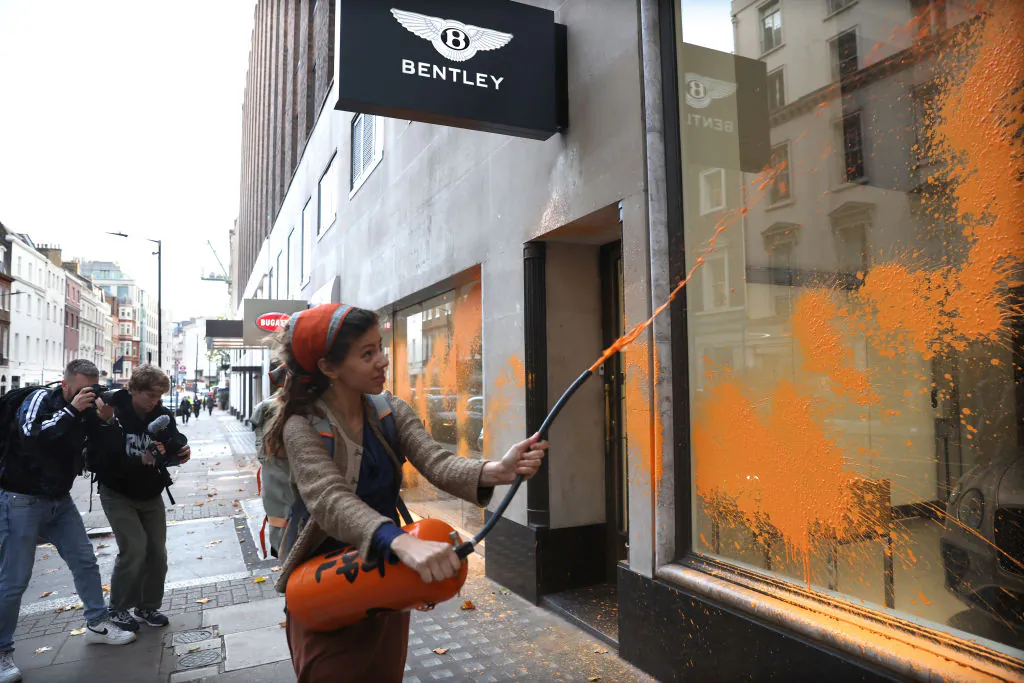 A demonstrator from Just Stop Oil sprays orange paint on the Jack Barclay Bentley store in Berkeley Square, in London, on Oct. 26, 2022. The protest group has organized a wave of similar actions across London in recent weeks. (Photo by Isabel Infantes/Getty Images)