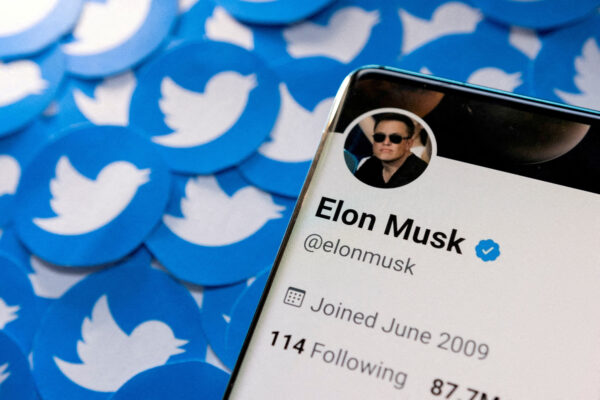 Elon Musk's Twitter profile on smartphone and printed Twitter logos