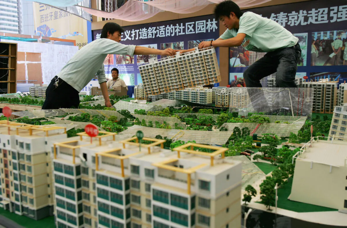 Two workers move a building model during a real estate fair in Shaanxi Province, China, on April 18, 2007. (China Photos/Getty Images)