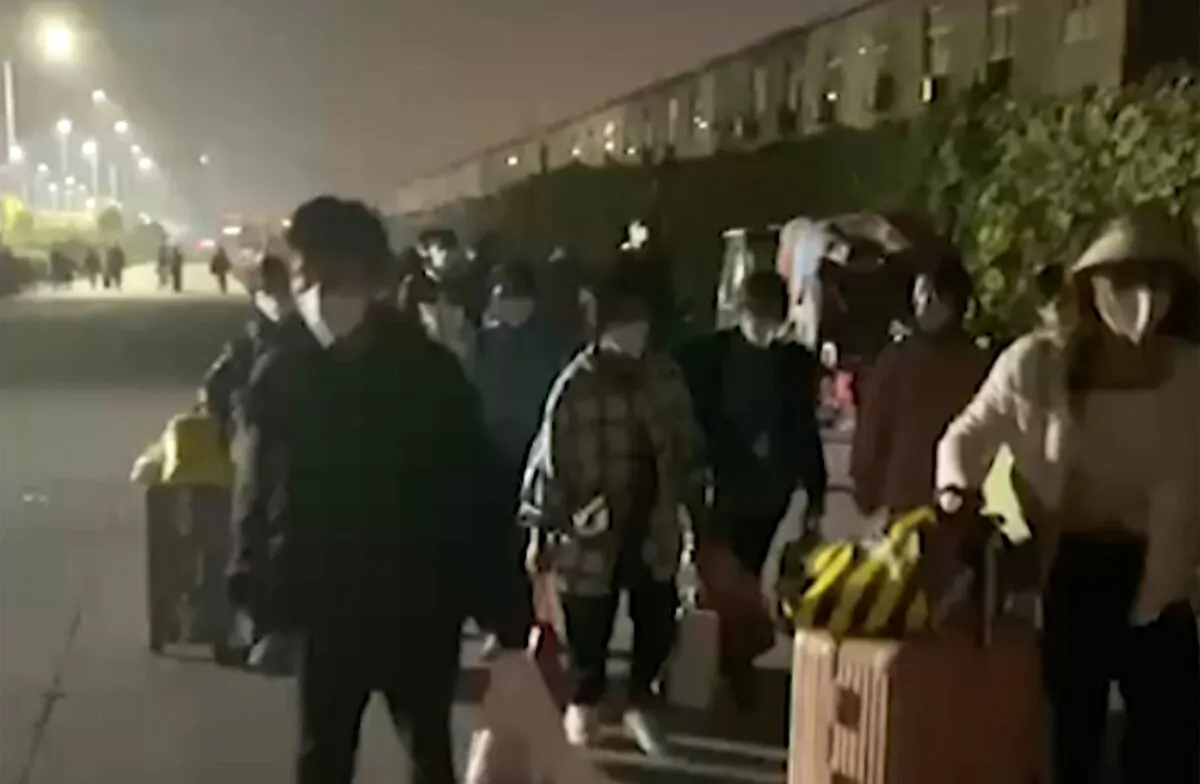People with suitcases and bags leave from a Foxconn compound in Zhengzhou in central China's Henan Province on Oct. 29, 2022, in a still from video. (Hangpai Xingyang via AP)