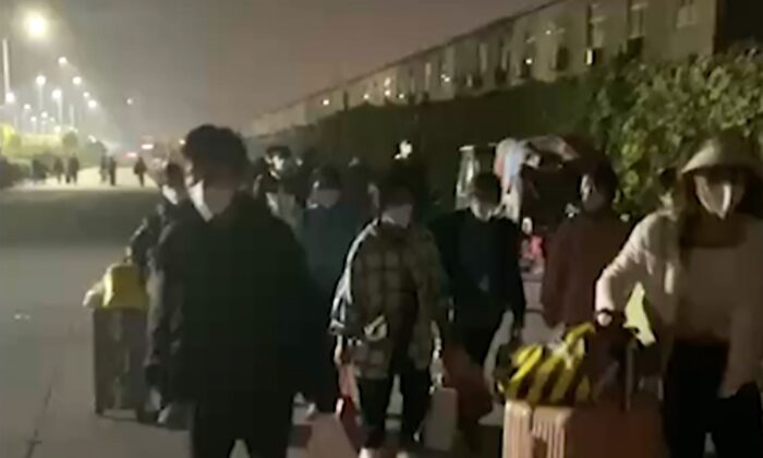 在这张由航拍星阳发布的视频片段中拍摄的照片中，2022 年 10 月 29 日，人们带着手提箱和行李离开河南省郑州的富士康大院。（航拍星阳/美联社截图）

