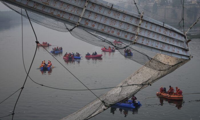 2022 年 10 月 31 日，救援人员乘船在印度西部古吉拉特邦莫尔比镇倒塌的索桥旁的马赫楚河中搜寻。（Ajit Solanki/美联社照片）