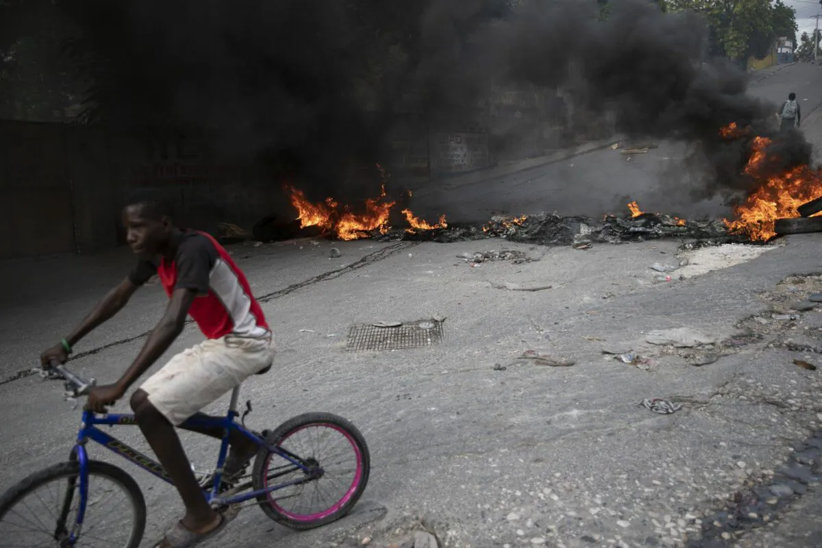 A man rides his bicycle a burning barricade during a protest over the death of journalist Romelo Vilsaint, in Port-au-Prince, Haiti, Oct. 30, 2022. (The Canadian Press/Odelyn Joseph)