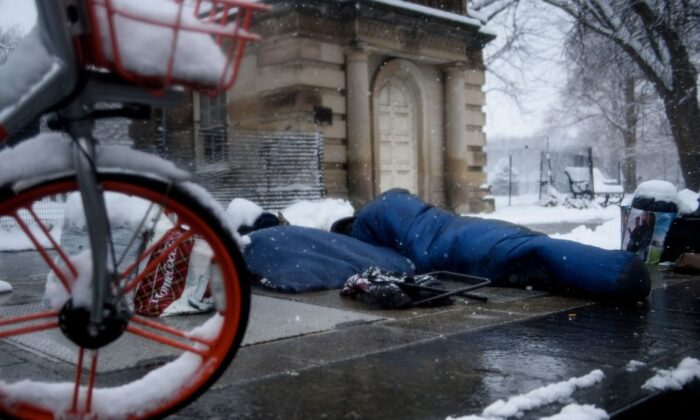 2019 年 1 月 13 日，华盛顿特区的一场冬季风暴期间，一名无家可归的男子在白宫附近的暖风口上方休息。（Brendan Smialowski/AFP via Getty Images）