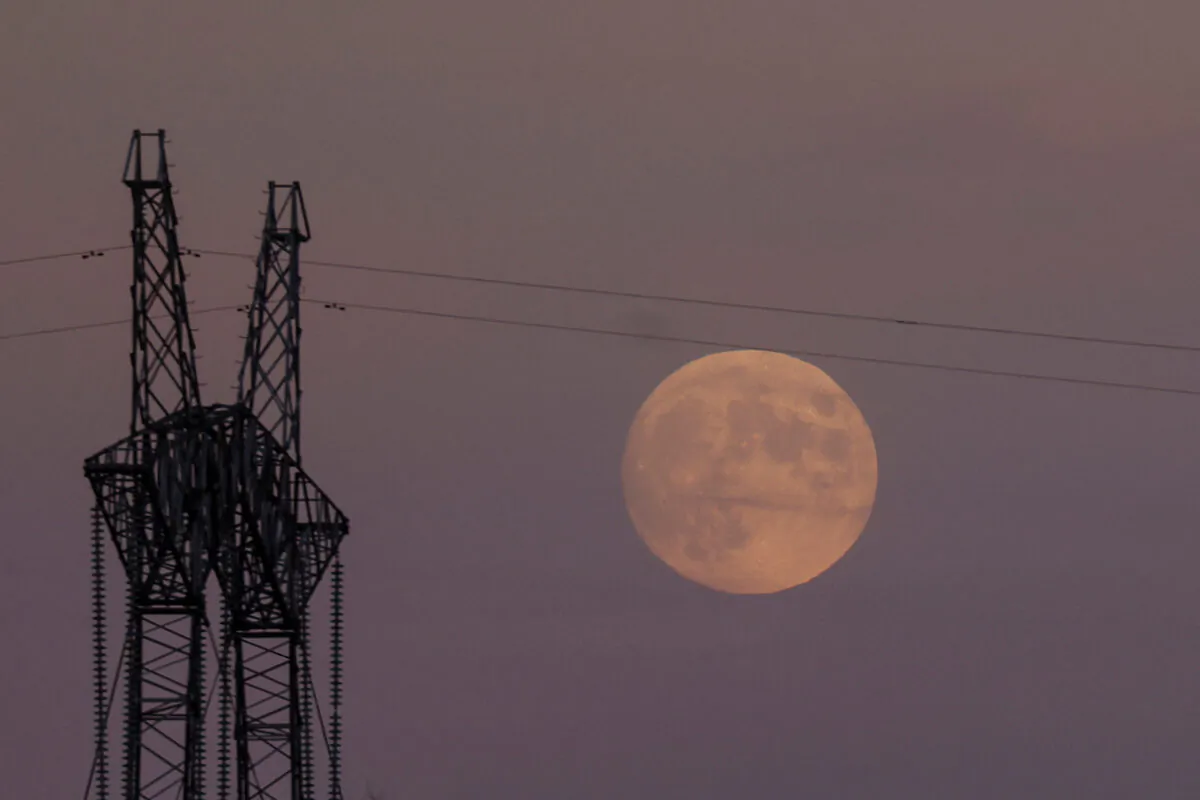 A full moon rises behind an electricity pylon with high-voltage power lines in Dnipropetrovsk region, Ukraine, on Nov. 7, 2022. (Valentyn Ogirenko/Reuters)