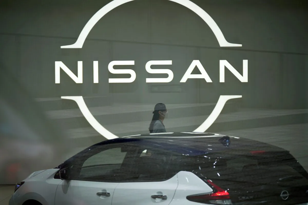 A staff walking near a Nissan logo at Nissan headquarters though a window in Yokohama near Tokyo on May 12, 2022. (Eugene Hoshiko/AP Photo)