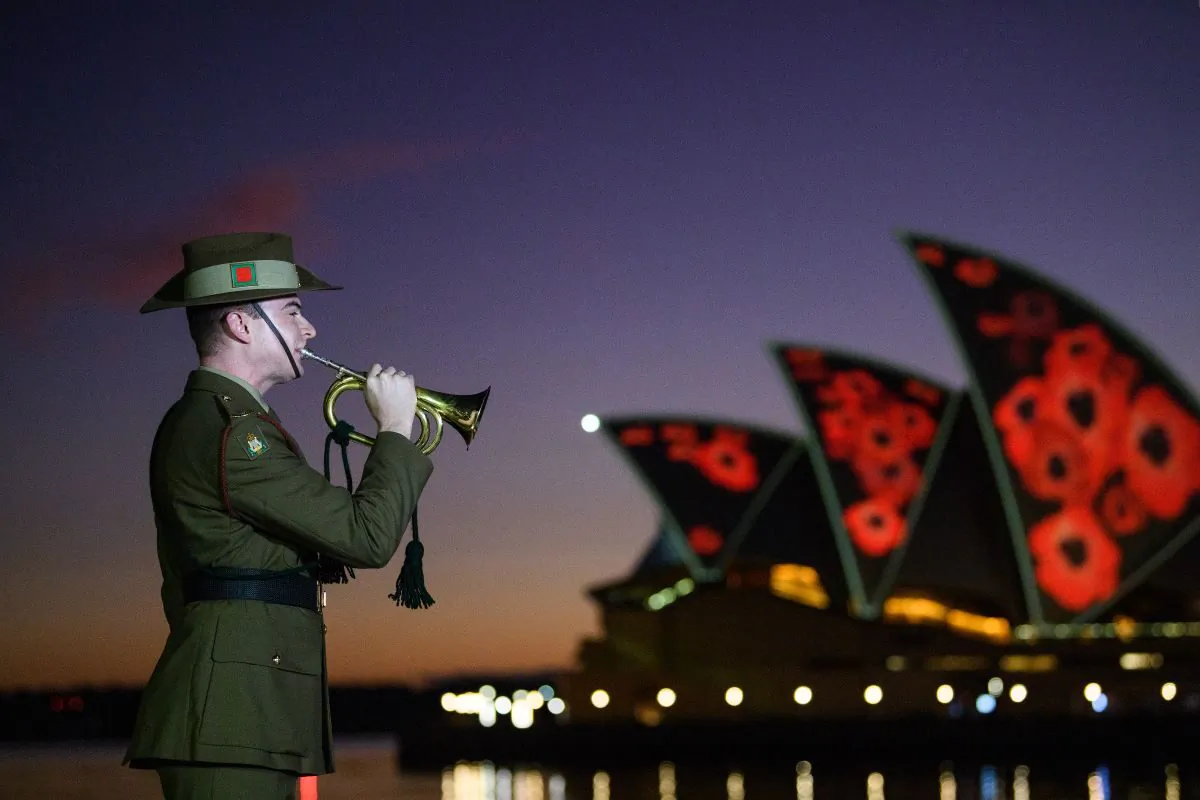 An Australian Defence Force (ADF) bugler plays ‘The Last Post’ as poppies are projected on to the Sydney Opera House sails during a Remembrance Day 2022 Dawn Service at Campbells Cove, in Sydney, November 11, 2022. (AAP Image/Bianca De Marchi)