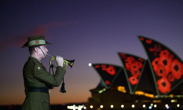 2022 年 11 月 11 日星期五，在悉尼坎贝尔湾举行的 2022 年阵亡将士纪念日黎明仪式期间，澳大利亚国防军 (ADF) 号手演奏“最后的帖子”，罂粟被投射到悉尼歌剧院的帆上。（AAP 图片/比安卡·德·马尔奇）
