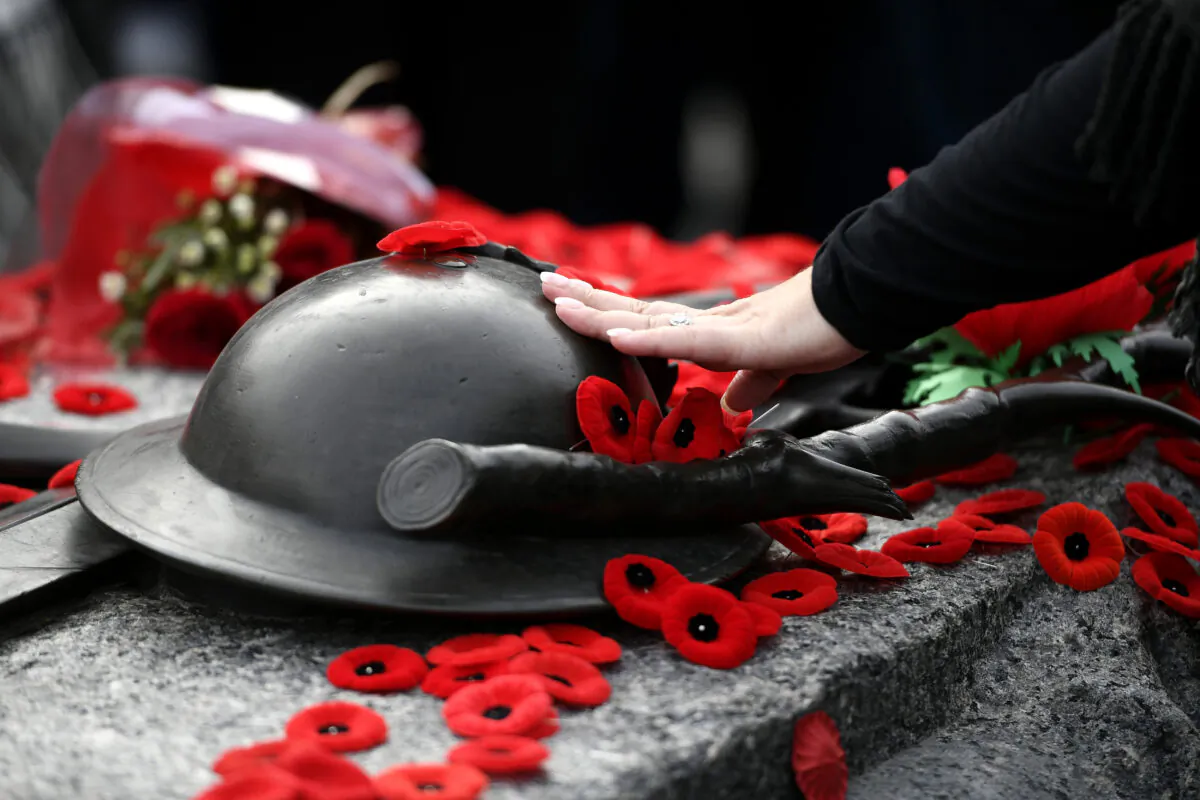 A person touches the helmet on the Tomb of the Unknown Soldier after laying a poppy, at the National War Memorial following the National Remembrance Day Ceremony in Ottawa on Nov. 11, 2022. (The Canadian Press/Justin Tang)