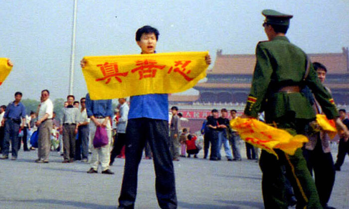 A Chinese policeman approaches a Falun Gong practitioner at Tiananmen Square in Beijing as he holds a banner with the Chinese characters for “truthfulness, compassion, and tolerance,” the core tenets of Falun Gong. (Courtesy of Minghui.org)