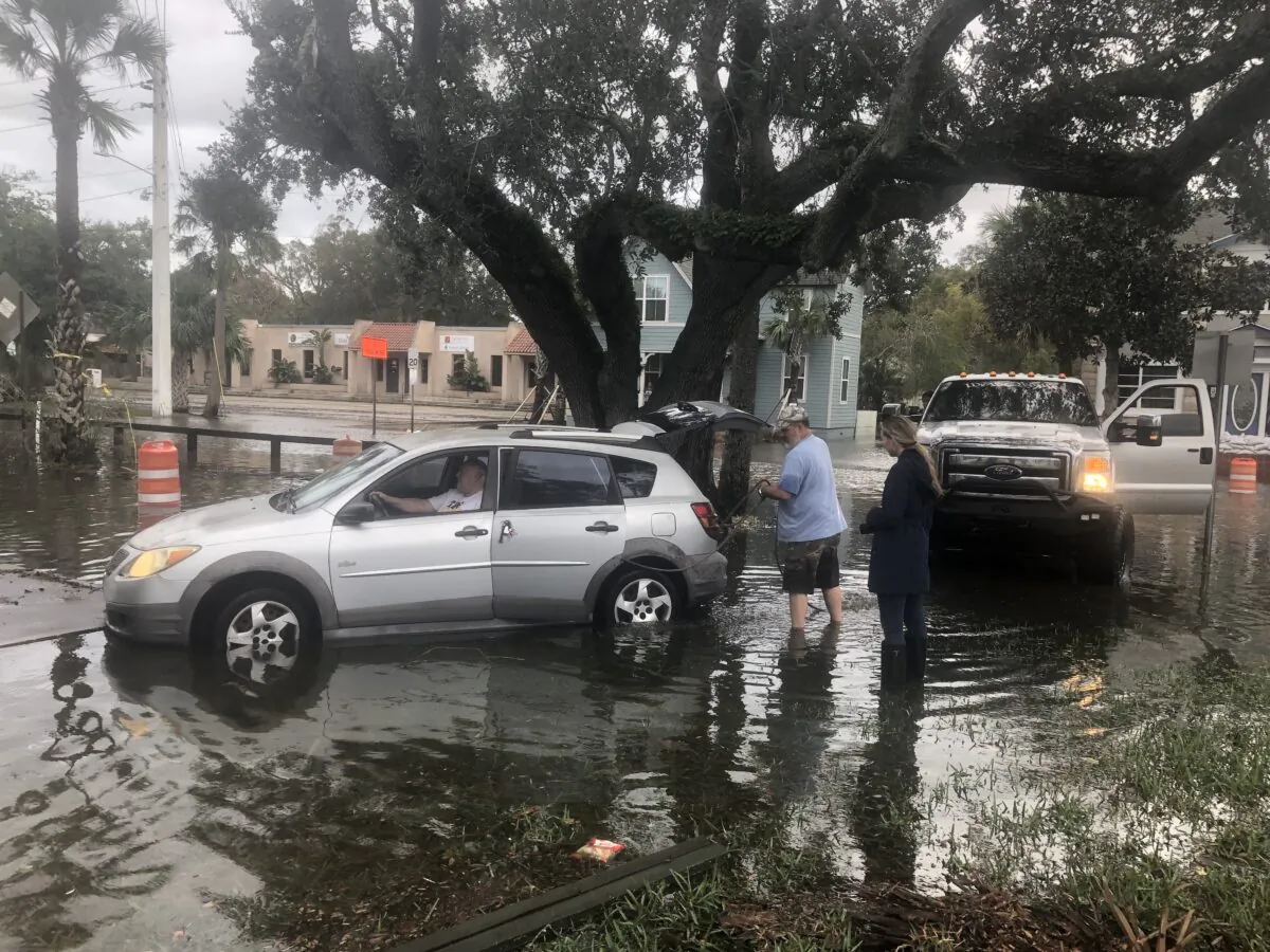 As floodwaters on a street in St. Augustine, Fla., swiftly recede, passerby Todd Schultz works to dislodge a stranger's sedan from a concrete platform that a half-hour earlier had been hidden by the coffee-colored water. (Nanette Holt/The Epoch Times) 