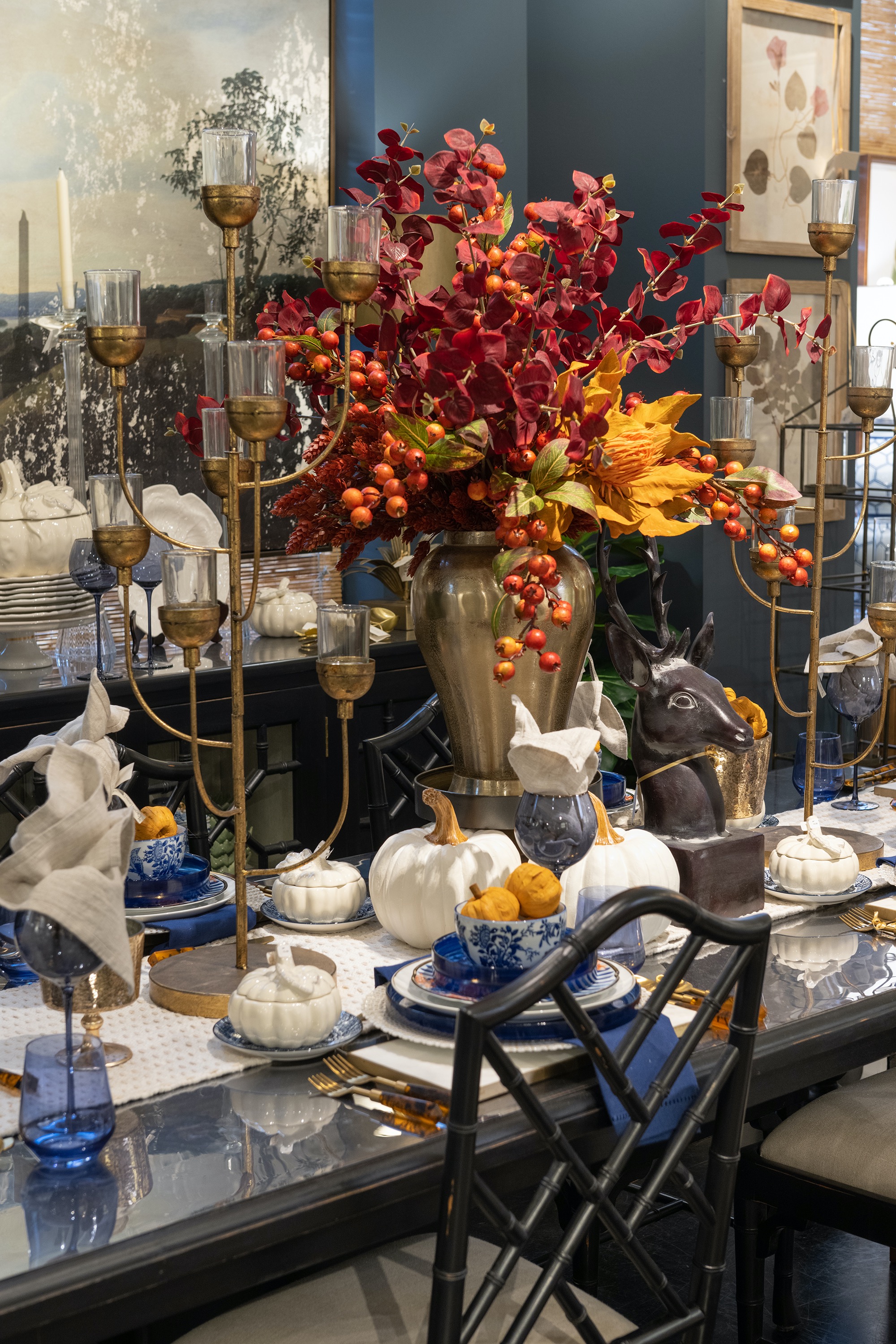A Thanksgiving tabletop awaits guests with a tall floral centerpiece flanked by candlesticks amid a sea of white pumpkins.