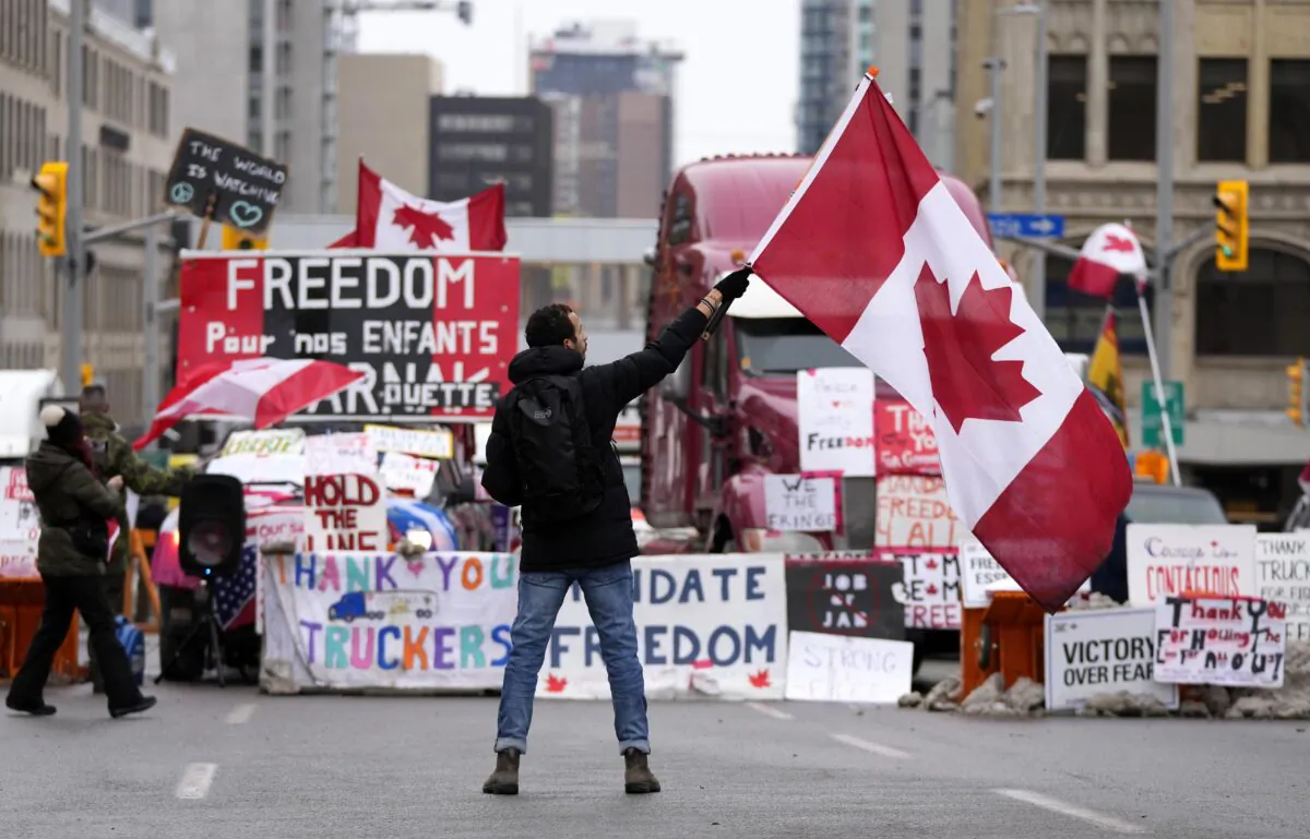 A protester waves a Canadian flag in front of parked vehicles on Rideau Street on the 15th day of the Freedom Convoy protest against federal COVID-19 mandates and restrictions in Ottawa on Feb. 11, 2022. (Justin Tang/The Canadian Press)